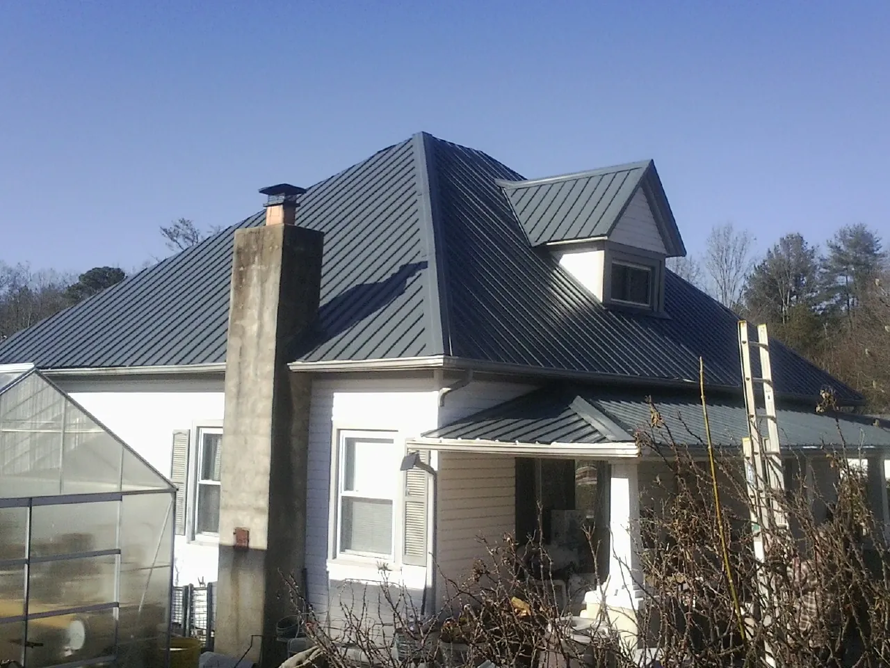 Dark blue standing seam metal roof on a white farmhouse with dormer — Slate & Tile Roof Repair by Roofing Brothers in Horse Branch