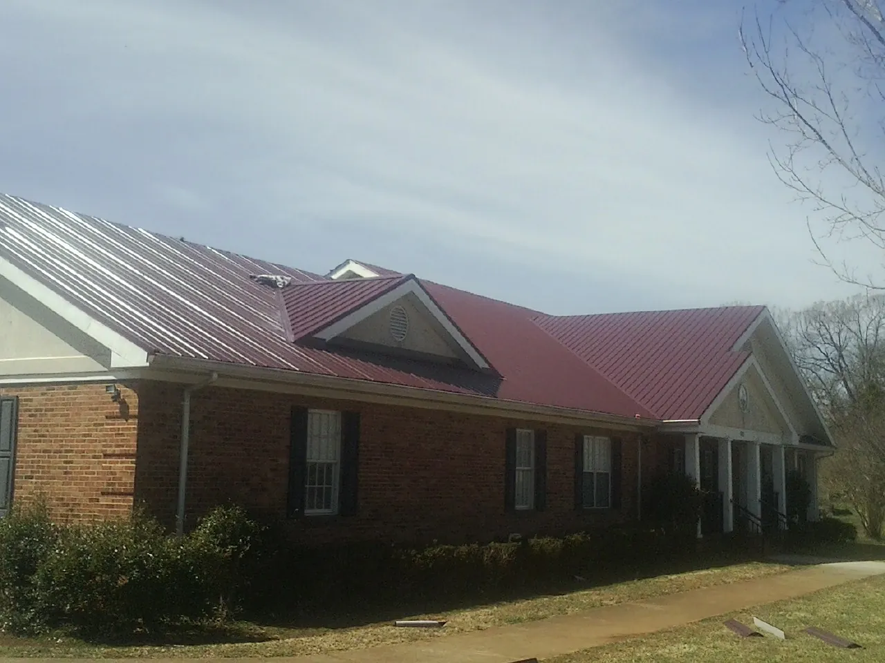 Red metal roof with gabled entries on a long brick building, from a Hail Damage Roof Repair job in Horse Branch