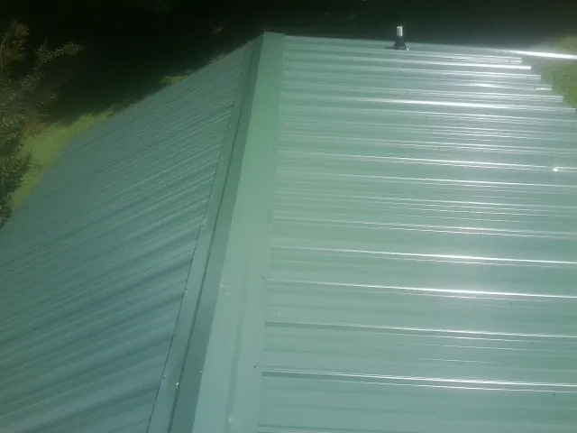 New green metal panels meeting at the ridge of a roof — Flat Roof Repair work by our crew in Horse Branch
