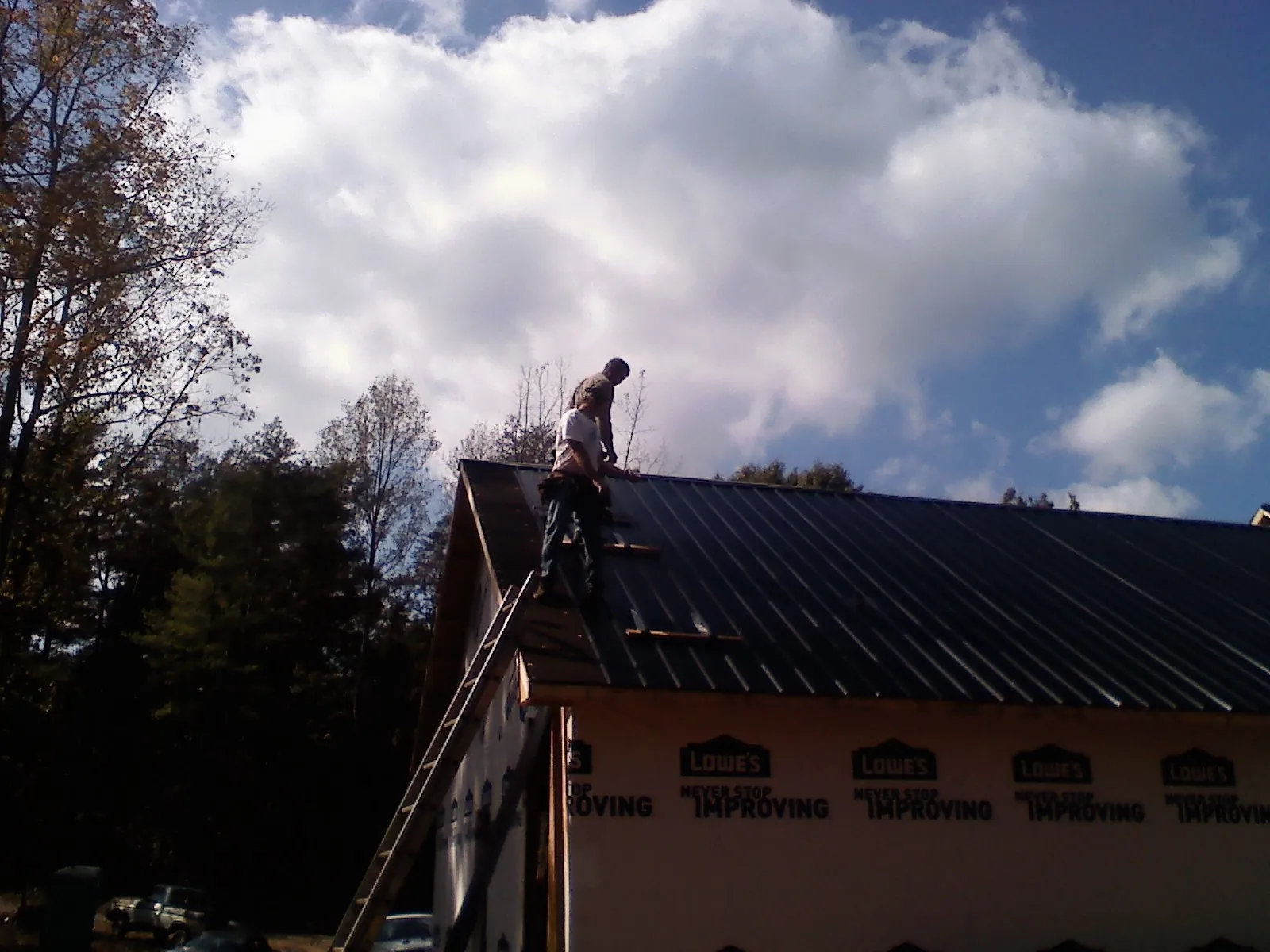 Roofer fastening dark metal panels high against a cloudy sky, from a Roof Inspection job in Horse Branch