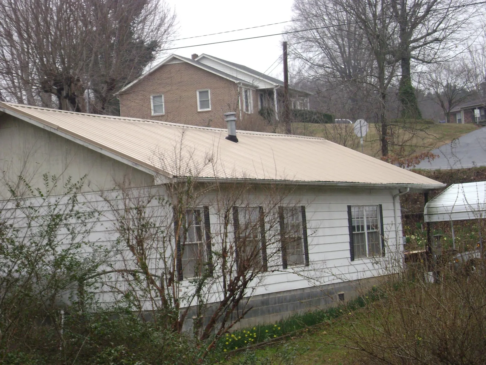 Tan metal roof on a white sided house set into a hillside — Commercial Roofing by Roofing Brothers in Horse Branch