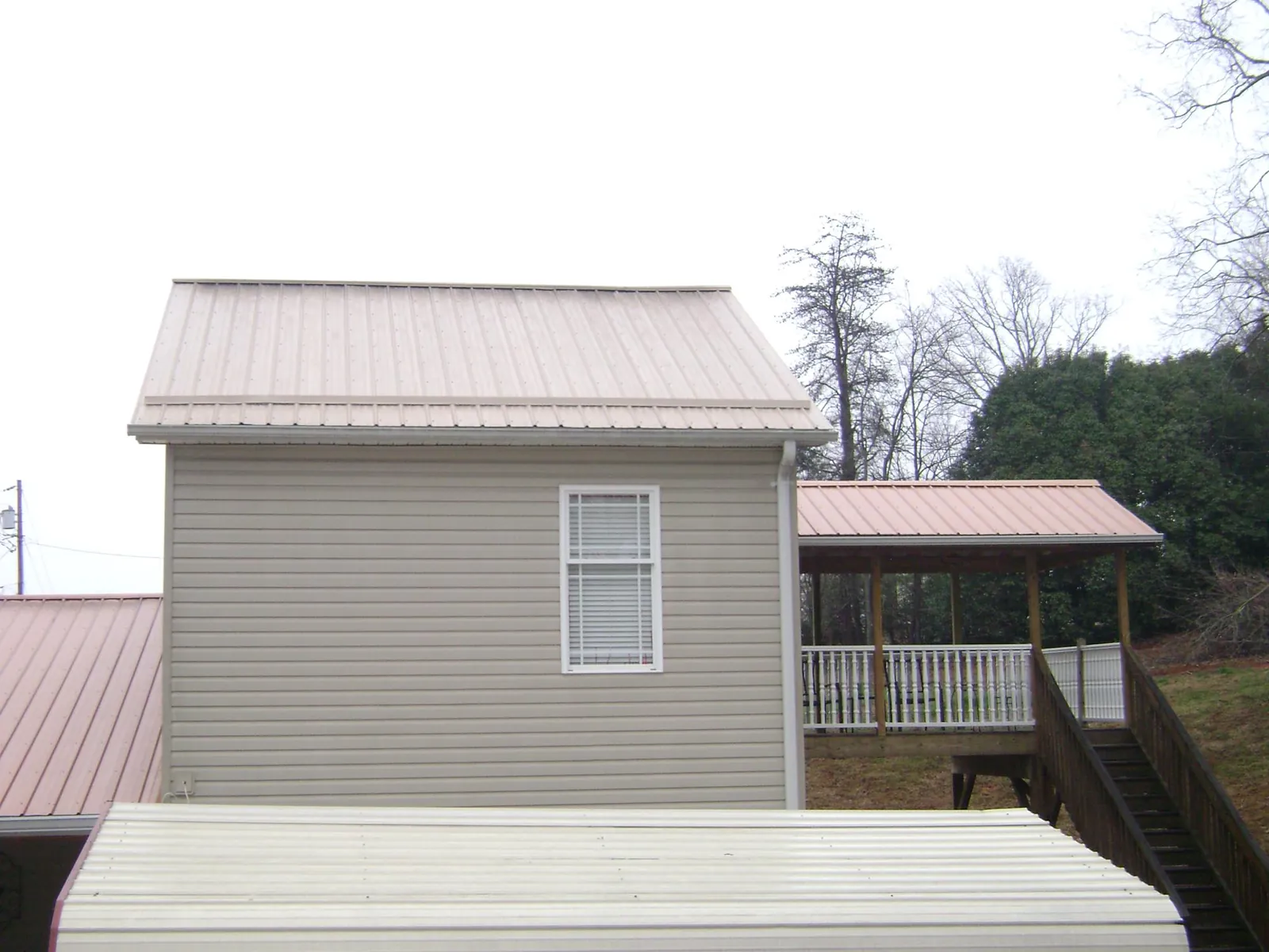 Tan metal roofs on a two story addition and attached porch, from a Roof Replacement job in Horse Branch